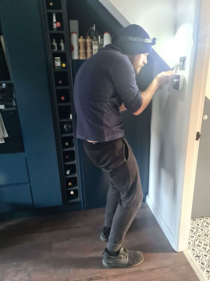 Man displaying awkward body language while adjusting thermostat in modern kitchen setting, illustrating awkward body language.