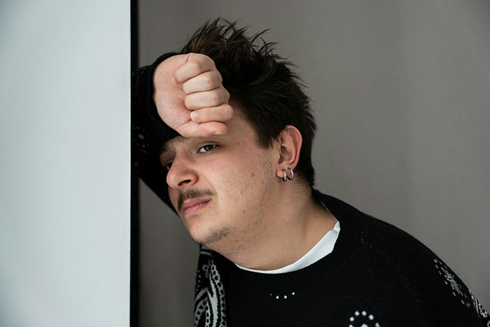 Young man leaning against a wall looking distressed, reflecting on family kidney request after betrayal and loss.