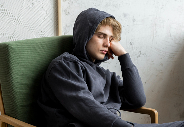 Young man in a dark hoodie sitting with eyes closed, reflecting on major family chaos after DNA test results.