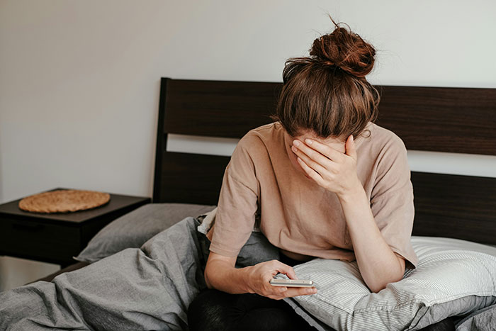Woman sitting on bed, looking stressed and covering face, reflecting on being child-free and family conflicts.