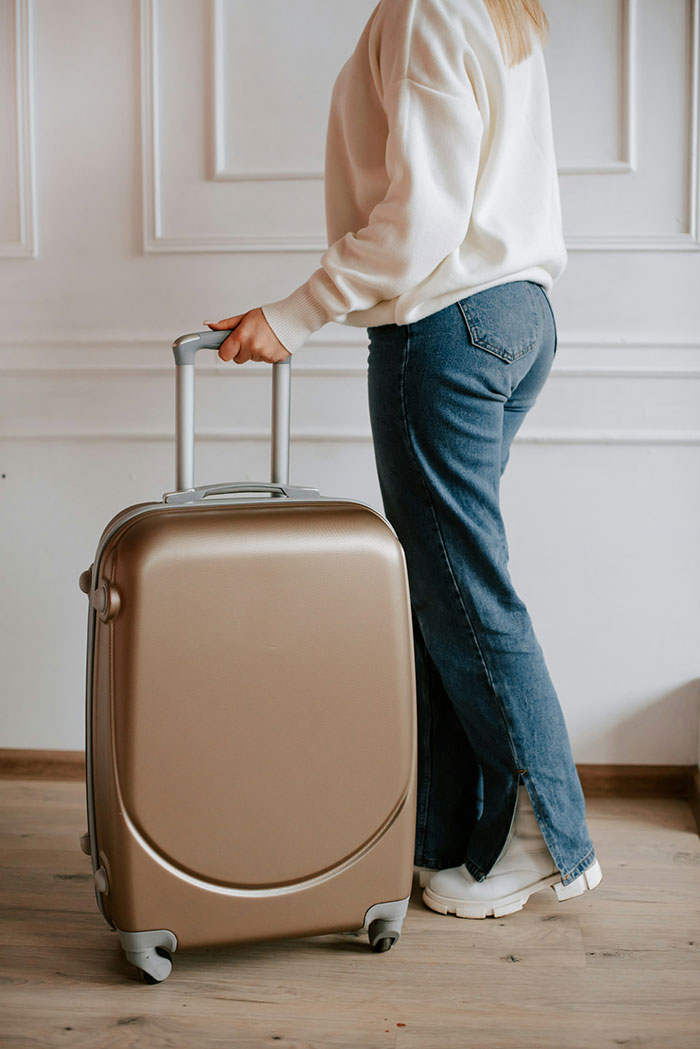 Woman standing indoors with suitcase, symbolizing refusal to house sister and child-free lifestyle decision.