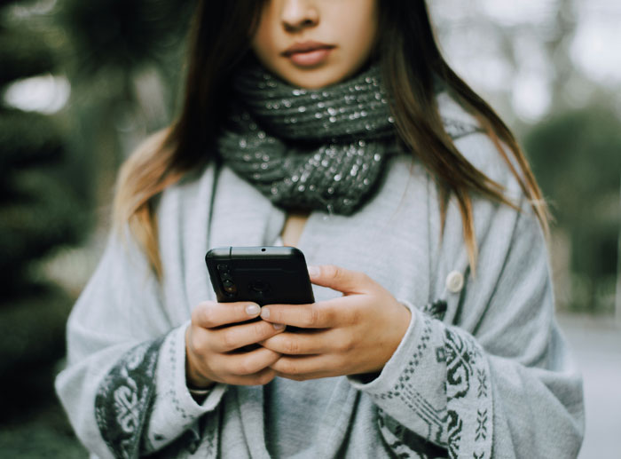 Young woman wrapped in a scarf focused on her phone, reflecting the tension of mom not letting sister have one conversation.