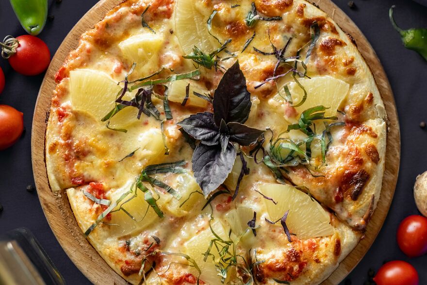 Close-up of a pineapple pizza on a wooden board, illustrating one of the top pet peeves that instantly divide a room.