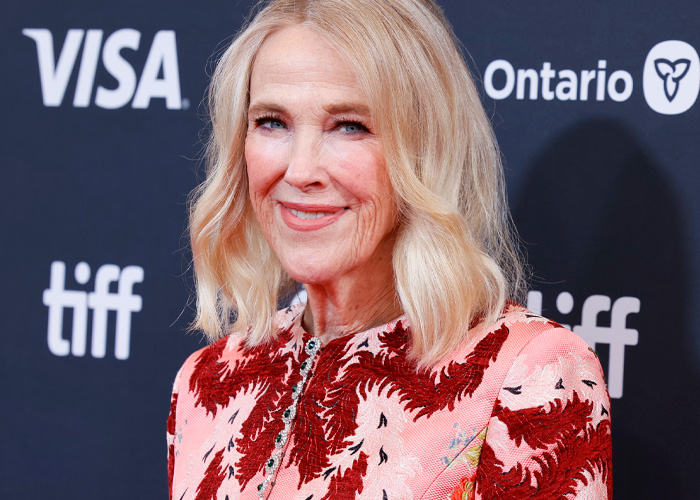 Catherine O'Hara smiling in a red and pink floral outfit at a TIFF event, related to cause of passing news.