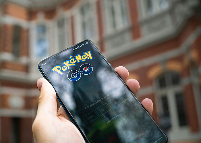 Mobile game players holding smartphone with Pok&eacute;mon Go app open, highlighting controversy around in-game locations.