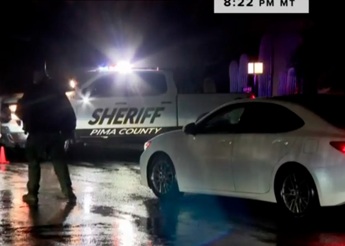 Police officer near sheriff vehicle and white car at night investigating Nancy Guthrie kidnapper pivotal moment case scene.