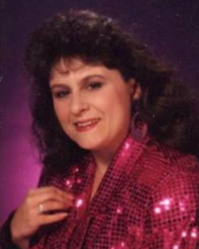 Woman in a pink sequined jacket posing against a dark purple background in a photo linked to a mom who vanished 25 years ago.