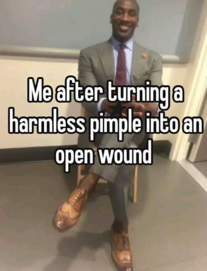 Man in a suit smiling while sitting with legs crossed, paired with a random meme about pimples and entertaining humor.