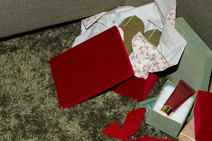 Red velvet gift boxes with tissue paper and a red tube of lotion on a green s**g carpet, illustrating belongings usage.