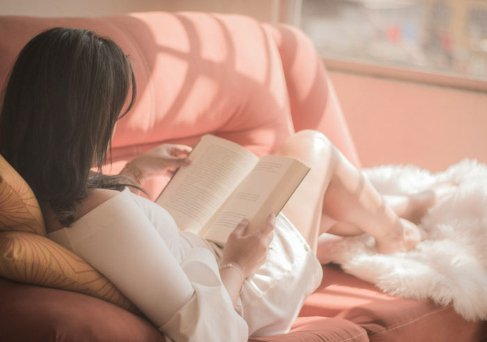 Woman relaxing on a couch reading spicy books, enjoying her time immersed in the story in a cozy setting.