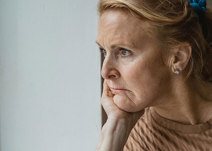 Middle-aged woman looking out window pensively, reflecting on family conflict and lifestyle issues involving CPS.