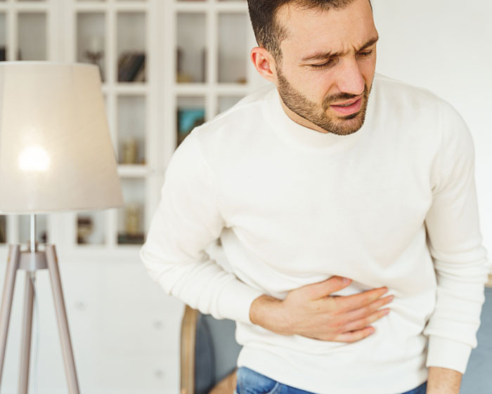 Man in a white shirt holding his stomach in pain, illustrating healthcare workers' experiences and challenges seen firsthand.