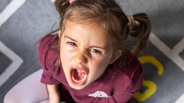 Young girl with pigtails shouting angrily, expressing strong emotions after being shamed in front of everyone.