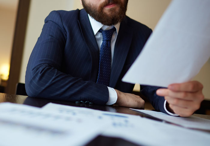 Man in a suit reviewing inheritance documents at a desk, symbolizing conflict over late husband's estate and family issues.