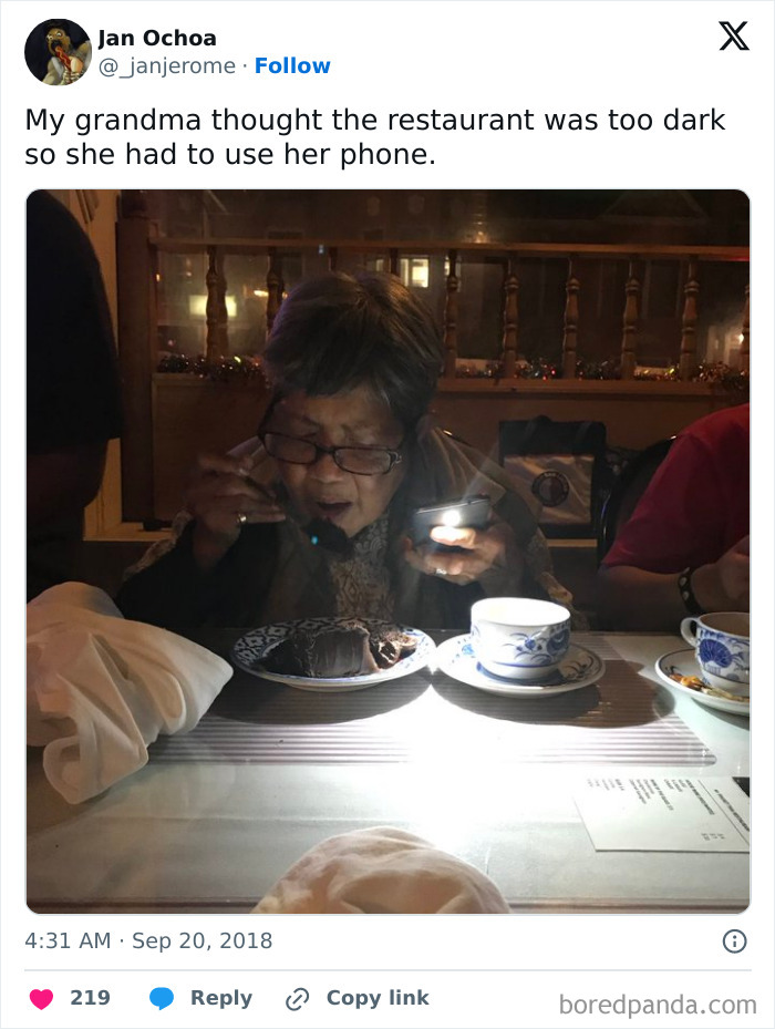 Elderly woman using phone light to eat in a restaurant, showcasing boomers trying technology and failing miserably.