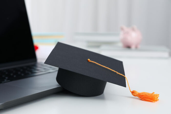 Graduation cap with an orange tassel placed next to a laptop, symbolizing wake-up calls and life decisions.