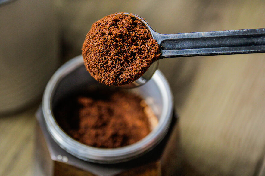 Close-up of ground coffee in a measuring spoon above a jar, showcasing everyday items in creative life hacks.