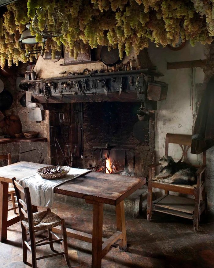 Rustic bold interior with wooden table, hanging dried flowers, stone fireplace, and cozy vintage chair with a dog.