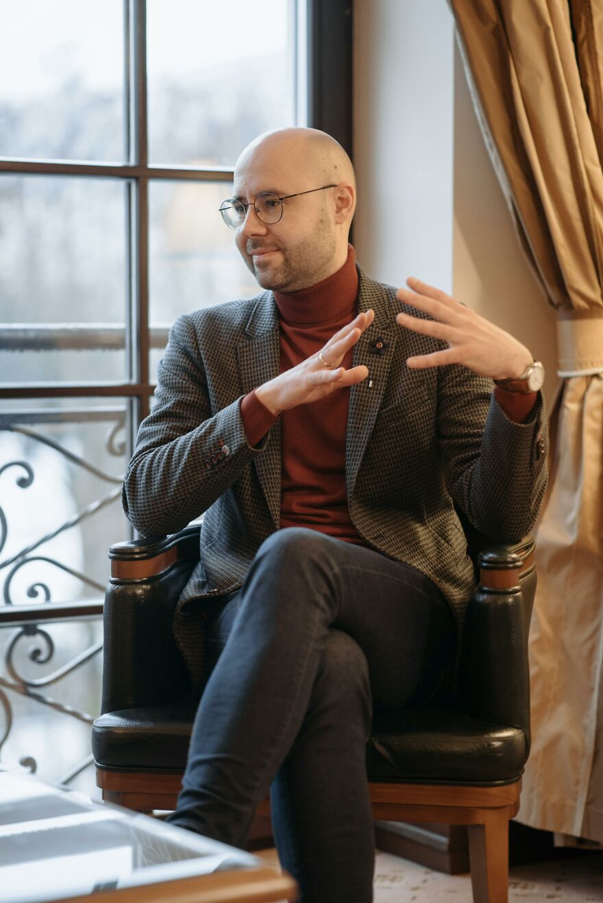 Man in glasses and blazer sitting and gesturing while discussing common pet peeves that divide a room indoors.