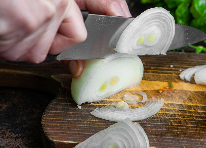 Hand slicing onion on wooden cutting board demonstrating quick fix cooking technique that turned out genius solution.