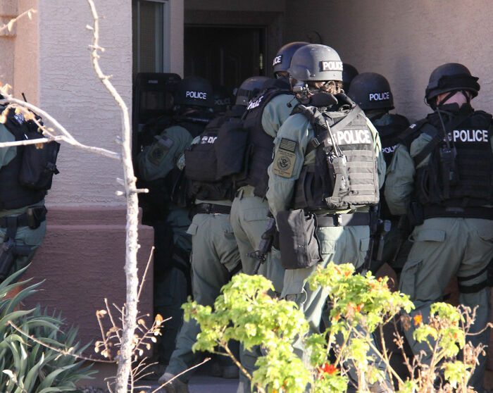 Police officers in tactical gear preparing to enter a building amid major update in Alex Pretti's case medical examiner's ruling.