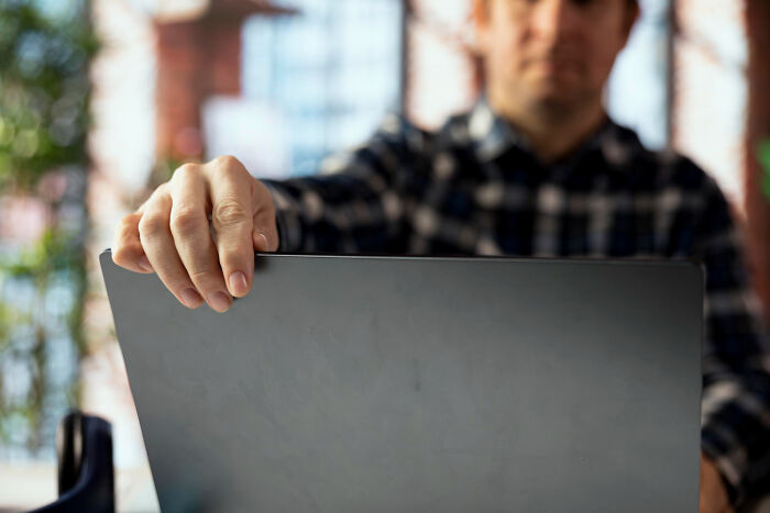 Man in a checkered shirt holding a laptop, symbolizing brutal wake-up calls to escape a nasty situation immediately.