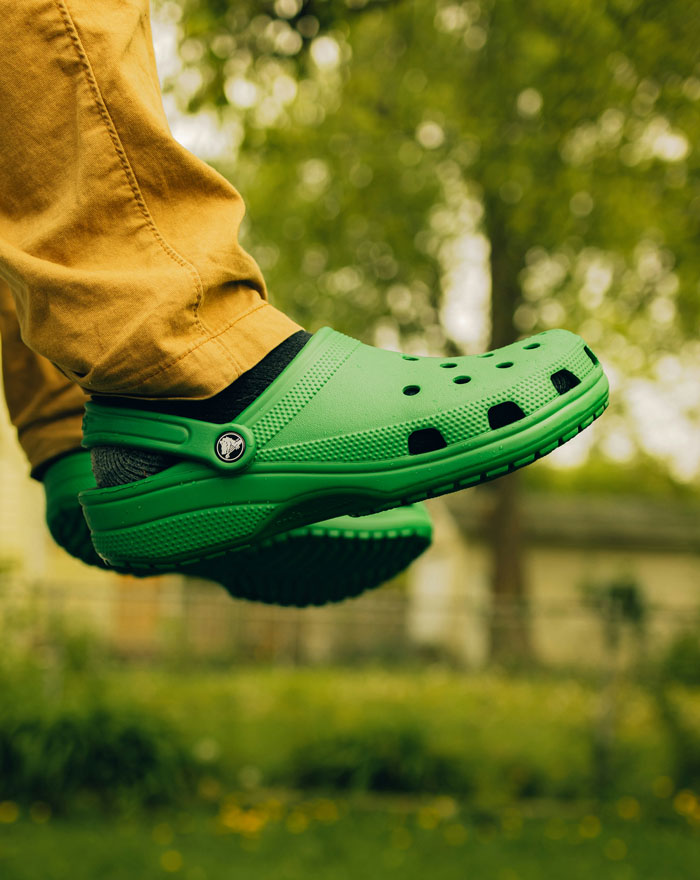 Person wearing green clogs and brown pants outdoors with blurred greenery in background, symbolizing healthcare workers' experiences.