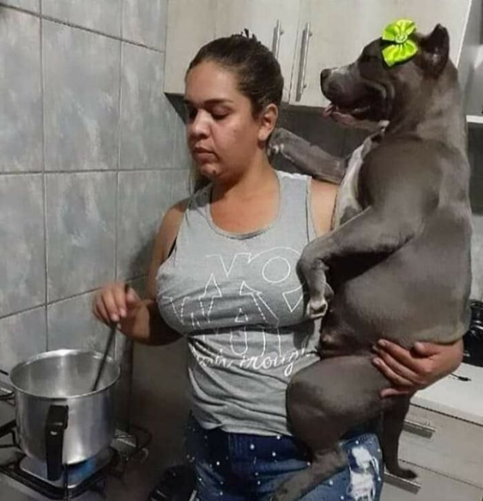 Woman holding a dog wearing a green bow while cooking, showing an unexpectedly beautiful bond between humans and animals.