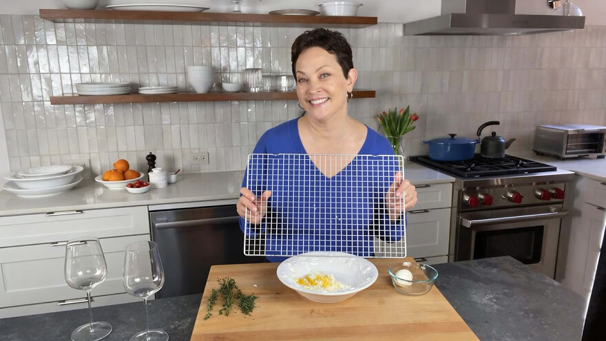 Woman in a modern kitchen demonstrating genius hacks using everyday items with a cooling rack and cooking ingredients on the counter.
