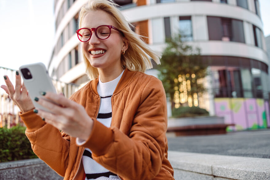 Young woman smiling and using smartphone outdoors, illustrating common pet peeves that divide a room.