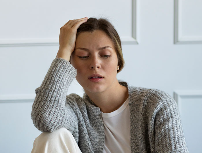 Young woman looking stressed and tired, wearing a gray sweater and white shirt, reflecting on challenges of longer shifts.