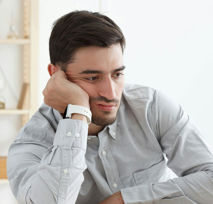 Man in a gray shirt looking distraught while resting his head on his hand, reflecting on a wife&rsquo;s secret exposed after childbirth.