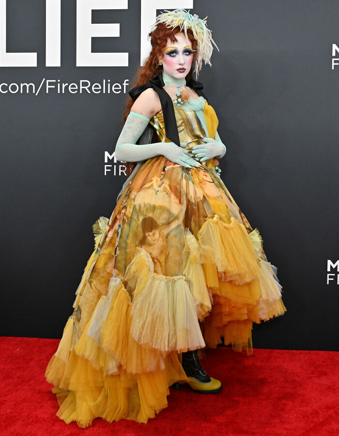 Chappell Roan in a bold, artistic yellow gown with dramatic makeup on the red carpet at a formal event.