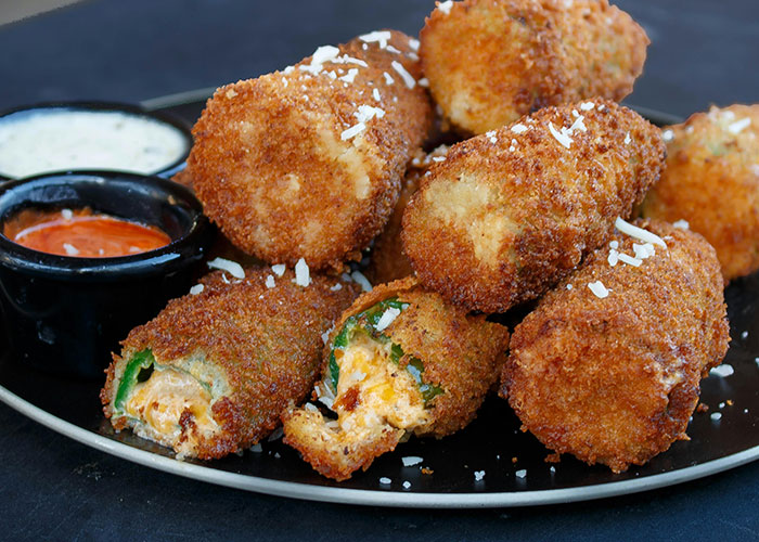 Close-up of crispy fried jalapeno poppers with cheese filling served on a black plate with dipping sauces, related to messed up stories.