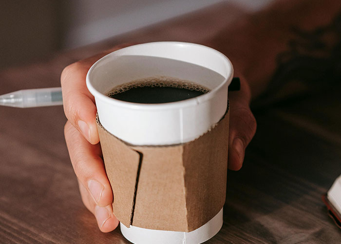Hand holding a paper cup of coffee, representing moments from Today I Messed Up stories to feel better about life.