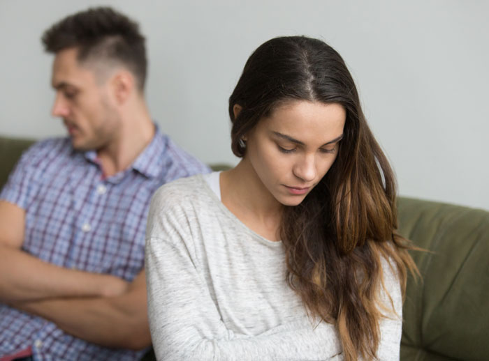 Upset wife and husband sitting apart on couch after wife&rsquo;s secret exposed following birth of a black child.