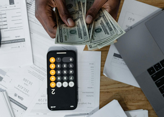 Hands counting US dollars over a desk with bills, receipts, and a calculator app, illustrating smart money habits worldwide.