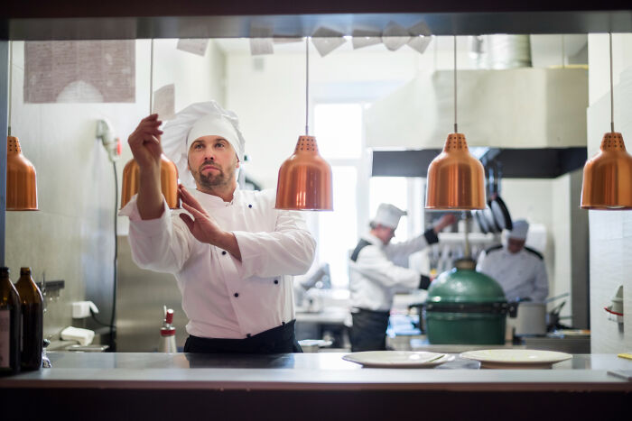 Chef in professional kitchen wearing white uniform and hat, preparing food as a brutal wake-up call moment.