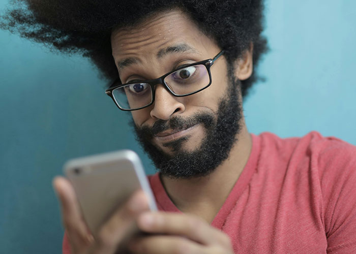 Man with glasses in a red shirt reacting to a phone, relatable today I messed up stories for comfort and humor
