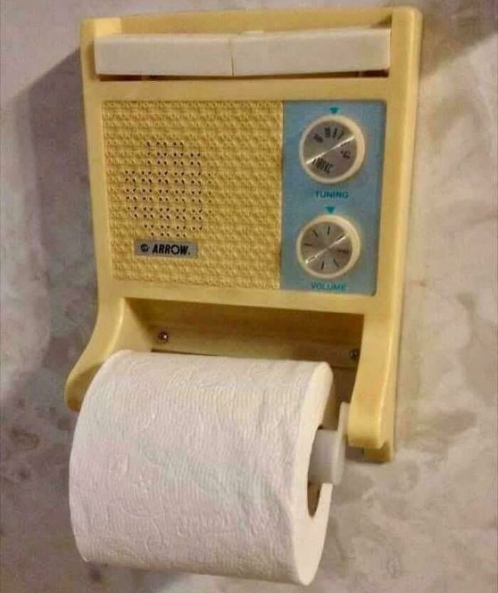 Vintage wall-mounted radio with tuning and volume dials combined with a toilet paper holder in a nostalgic bathroom setting