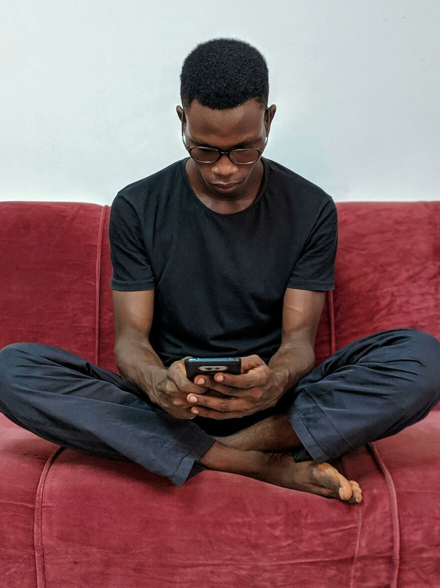 Young man sitting cross-legged on a red couch, focused on his phone, illustrating common pet peeves dividing a room.
