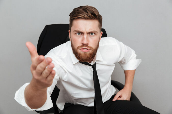 Angry man in white shirt and black tie making a strong wake-up call gesture in an office chair.