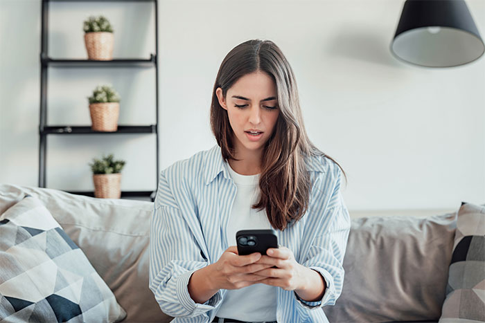 Young woman on a couch looks shocked while reading a message on her phone during a first date that goes horribly wrong.