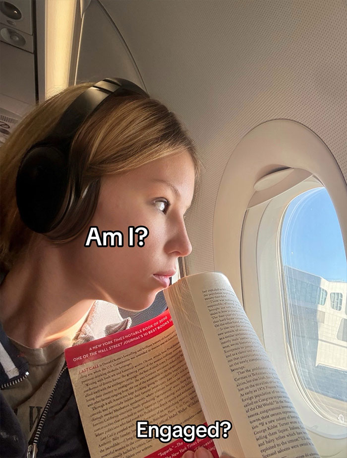Young woman wearing headphones, reading on a plane window seat during travel encounter with kind stranger viral story.