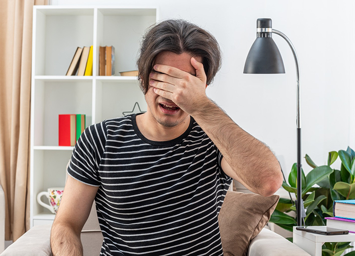 Young man frustrated and stressed, sitting on couch, refusing to help spoiled brother while parents are upset at home.