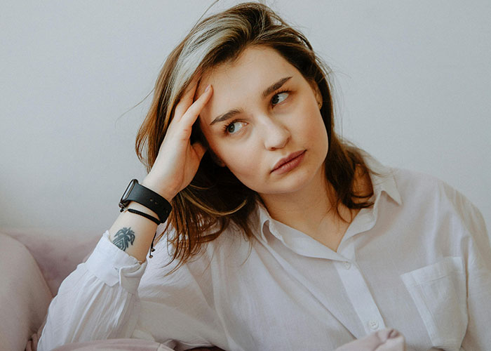 Young woman with a tattoo looks thoughtful and concerned, reflecting on family conflict and being a lesbian.
