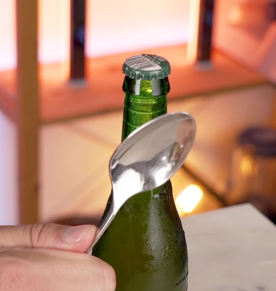 Hand holding a spoon to open a bottle cap, demonstrating everyday items used in genius hacks.