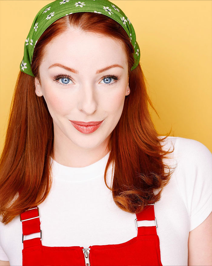 Red-haired woman wearing a green floral headband and red overalls, representing an Ex-Disneyland Evil Queen character.
