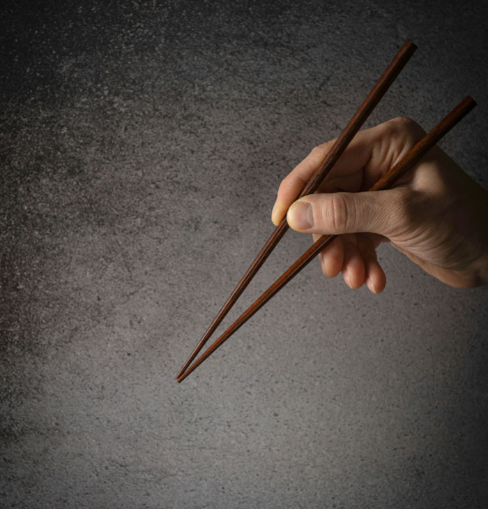 Hand holding wooden chopsticks demonstrating a quick fix technique in a minimalist setting.