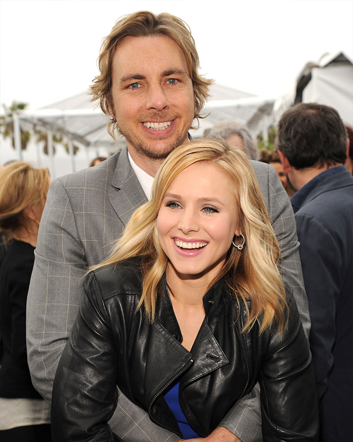 Dax Shepard and Kristen Bell smiling at an outdoor event with Dax Shepard embracing Kristen Bell from behind.